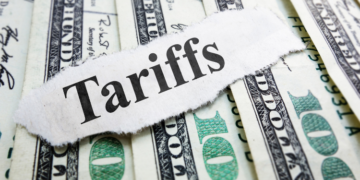 $100 bills laid out with the word "Tariffs" written over them.