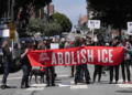 Protesters in the street holding a large red banner that reads "Abolish ICE".