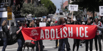 Protesters in the street holding a large red banner that reads "Abolish ICE".