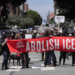 Protesters in the street holding a large red banner that reads "Abolish ICE".